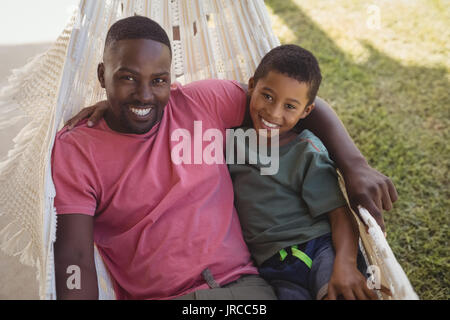 Portrait of smiling père et fils de vous détendre sur un hamac dans le jardin Banque D'Images