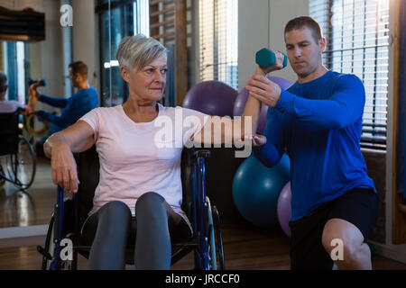 Physiothérapeute mâle helping patient dans l'exécution de l'exercice avec haltère dans clinic Banque D'Images