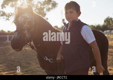 Garçon tenant les rênes d'un cheval dans le ranch sur une journée ensoleillée Banque D'Images