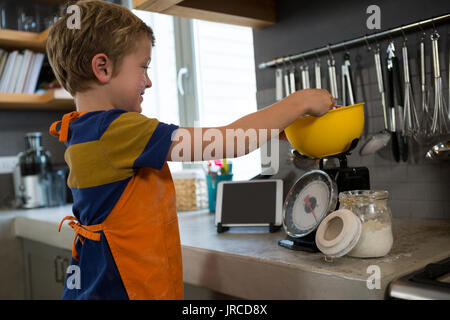 Boy Measuring food en jaune bol sur compteur à balance de cuisine Banque D'Images