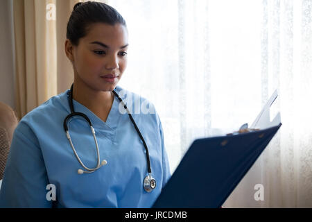 Femme médecin la lecture de rapports tout en se tenant par la fenêtre en maison de soins infirmiers Banque D'Images