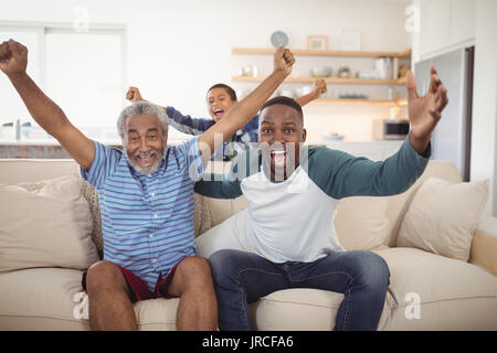 Acclamations de la famille tout en regardant la télévision dans la salle de séjour à la maison Banque D'Images