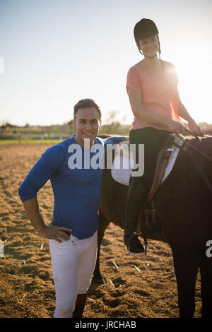 Portrait de trainer par young woman sitting on horse au barn Banque D'Images