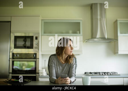 Woman tout en maintenant votre téléphone mobile en cuisine à la maison Banque D'Images