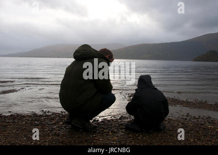 Un homme mûr et son jeune fils à la créatures au bord du Loch Lomond en Écosse. Banque D'Images