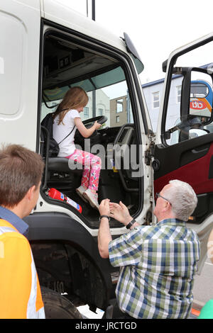 Une jeune fille est assise à la place de conduite d'un grand camion cabine à une démonstration de sécurité routière alors que son grand-père et le conducteur du camion. Banque D'Images