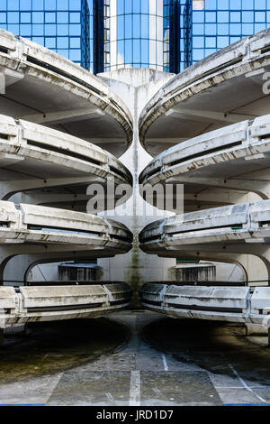 Rampes d'accès en spirale d'un vieux béton décrépit de parking, avec un immeuble de bureaux en verre à l'arrière-plan. Banque D'Images