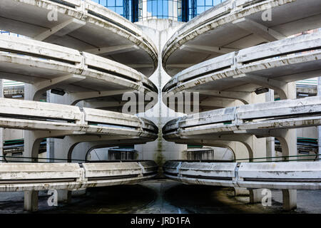 Rampes d'accès en spirale d'un vieux béton décrépit de parking, avec un immeuble de bureaux en verre à l'arrière-plan. Banque D'Images