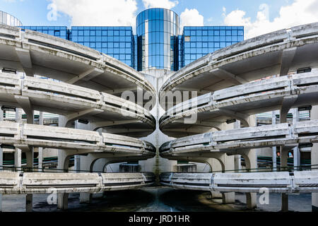 Rampes d'accès en spirale d'un vieux béton décrépit de parking, avec un immeuble de bureaux en verre à l'arrière-plan. Banque D'Images