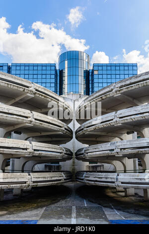 Rampes d'accès en spirale d'un vieux béton décrépit de parking, avec un immeuble de bureaux en verre à l'arrière-plan. Banque D'Images