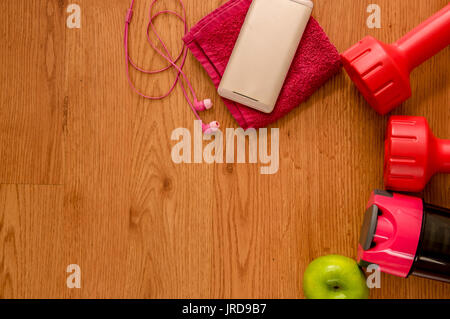 Jeu de l'athlète avec deux haltères rose smartphone, avec un casque rose sur une serviette rose, vert trouvera appple et une bouteille d'eau sur fond de bois. Banque D'Images