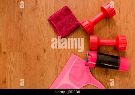 Jeu de l'athlète avec l'habillement femelle, rouge petite serviette, rose deux haltères courtes, bouteille d'eau et un soutien-gorge sport rose sur fond de bois. Banque D'Images