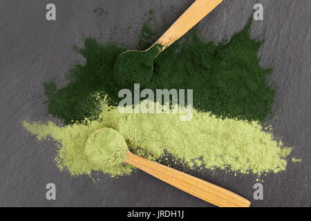 La Chlorella et l'orge en herbe, vert sain superfood poudre dans des cuillères en bois à partir de ci-dessus, la surface noire Banque D'Images