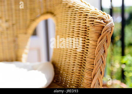 Une chaise en rotin, avec un coussin blanc dans la lumière du soleil à côté d'une fenêtre ouverte avec le semoir. Banque D'Images