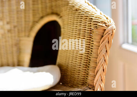 Une chaise en rotin, avec un coussin blanc dans la lumière du soleil à côté d'une fenêtre fermée. Banque D'Images