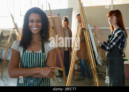 Portrait of smiling female artist avec vos amis la peinture dans la classe d'art à l'arrière-plan Banque D'Images