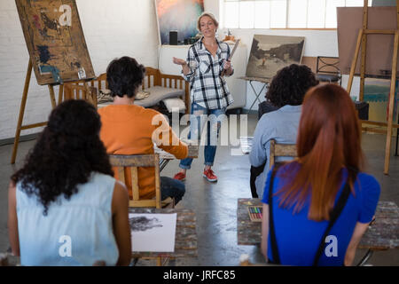 Les gestes de l'enseignant tout en expliquant aux étudiants assis à table dans la classe d'art Banque D'Images