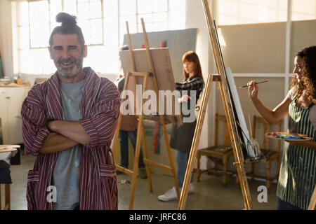 Portrait of smiling woman with arms crossed with painting in art class Banque D'Images