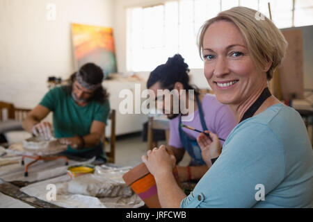 Portrait of female teacher decorating clay pot tout en rendant l'élève en classe d'art produits en argile Banque D'Images