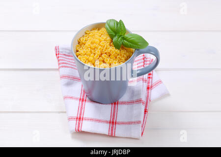 Tasse de petites coquilles de pâtes sur le torchon à carreaux Banque D'Images