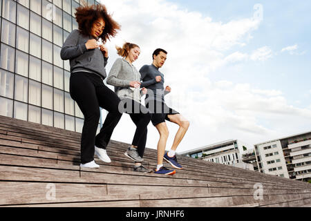 Trois jeunes gens actifs dans les vêtements de sport courir ensemble en bas, sur les escaliers de la ville Banque D'Images