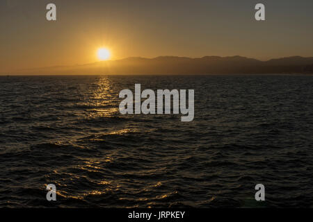 En el Anochecer oceano pacifico, en las pliayas de Santa Monica, el reflejo del sol en el agua, deja un camino de luz, atras se ven légères montañas Banque D'Images