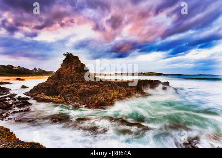 Maison falaise rocheuse érodée robuste off Kiama plage Bombo sur la côte pacifique de l'Australie au coucher du soleil avec un temps orageux. Banque D'Images