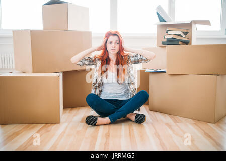 Tired woman sitting in yoga pose entre les boîtes de carton, pendaison. Réinstallation à new home Banque D'Images