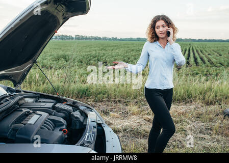 Jeune femme les appels vers le service d'urgence, casse de voiture. Problèmes avec véhicule sur route en journée d'été Banque D'Images