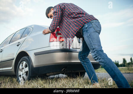 Man pushing casse voiture, vue de côté. Véhicule avec trounble sur route au jour d'été Banque D'Images