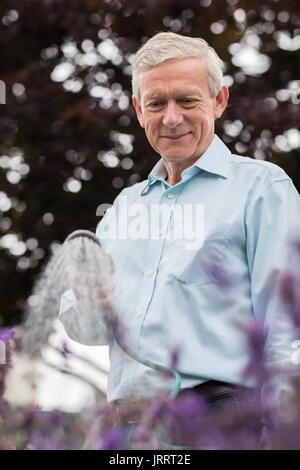 Senior Man Watering Flowers In Garden avec flexible Banque D'Images
