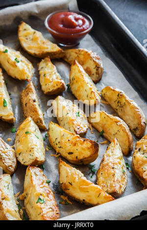 Quartiers de pommes de terre cuites au four avec des épices et herbes sur la plaque de cuisson - légumes bio faits maison végétarien végétalien les grignotines. Banque D'Images