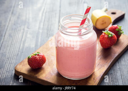 Smoothie fraise et banane sur fond de bois rustique. Petit-déjeuner ou une collation saine. Smoothie aux fraises et bananes dans un bocal en verre. Banque D'Images