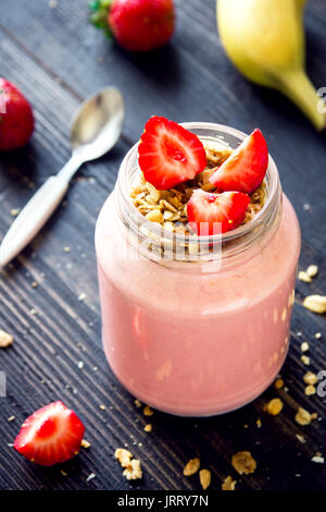 Smoothie fraise et banane avec granola fait maison. Petit-déjeuner ou une collation saine. Smoothie aux fraises et bananes dans un bocal en verre. Banque D'Images