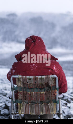 L'homme à la veste rouge se trouve sur l'ancien président dans la neige pendant qu'il observe le blizzard en face de lui. Banque D'Images