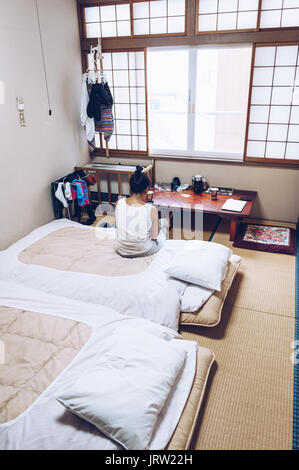 Jeune femme est assise sur le lit dans un ryokan Nozawa Onsen traditionnel en regardant par la fenêtre. Banque D'Images