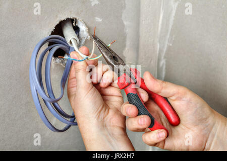 Les mains de l'électricien s'étirer le câblage à travers le trou dans le mur de la bande de plâtre, les câbles avant de les tirer. Banque D'Images