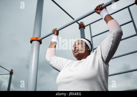 Déterminé l'embonpoint femme africaine La pratique de l'exercice à l'extérieur de pull-up Banque D'Images