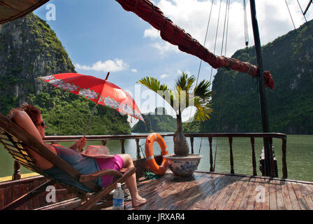 Les touristes à l'intérieur de détente une jonque chinoise, la baie d'Halong excursion en bateau de tourisme, Vietnam. junk, bateau naviguant entre les montagnes de calcaire karstique à cat ba nationa Banque D'Images
