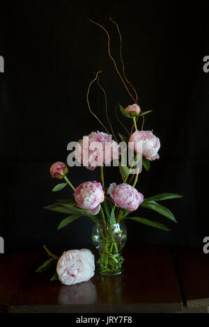 Les Pivoines rose dans un verre style roemer avec prunts sur une vieille table en bois avec fond noir Banque D'Images