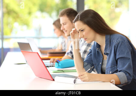 Vue latérale d'un étudiant concentré sur l'apprentissage en ligne dans une salle de classe avec ses camarades à l'arrière-plan Banque D'Images