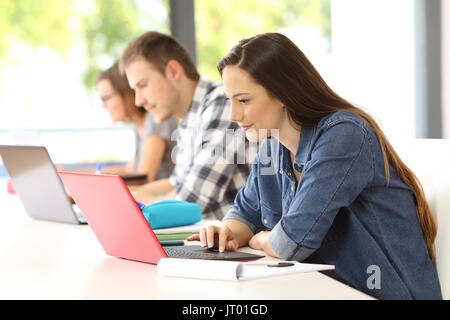 Vue de côté de trois étudiants attentifs sur l'apprentissage en ligne avec les portables assis dans une salle de classe Banque D'Images