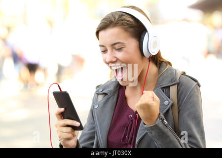 L'écoute des ados excités portant des écouteurs de musique sur un téléphone intelligent dans la rue Banque D'Images