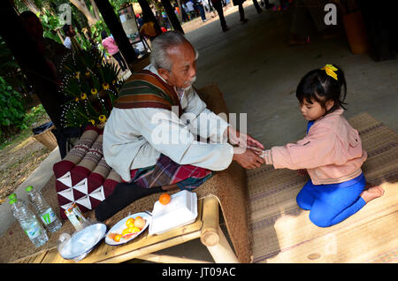 Vieil homme thaï thaï de liage du poignet pour cérémonie de bénédiction de la main girl at home le 30 décembre 2013 à Bangkok, Thaïlande Banque D'Images