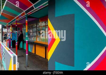 Personnes en attente d'un bus à l'intérieur d'un abri bus peintes de couleurs vives, Brighton, Sussex, UK Banque D'Images