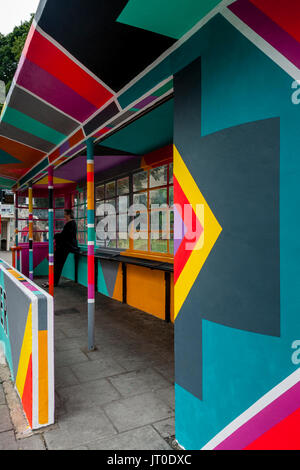 Personnes en attente d'un bus à l'intérieur d'un abri bus peintes de couleurs vives, Brighton, Sussex, UK Banque D'Images