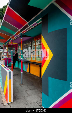 Personnes en attente d'un bus à l'intérieur d'un abri bus peintes de couleurs vives, Brighton, Sussex, UK Banque D'Images