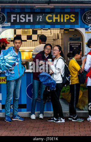 Les jeunes touristes à l'abri de la pluie à l'extérieur d'un poisson et Chip Shop sur le front de mer de Brighton, Brighton, Sussex, UK Banque D'Images