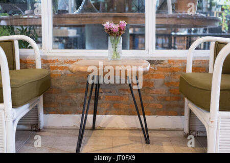 Siam tulip rose dans un vase de fleurs sur table en bois, en osier rotin blanc avec coussin chaise près de la fenêtre. Décoration Banque D'Images