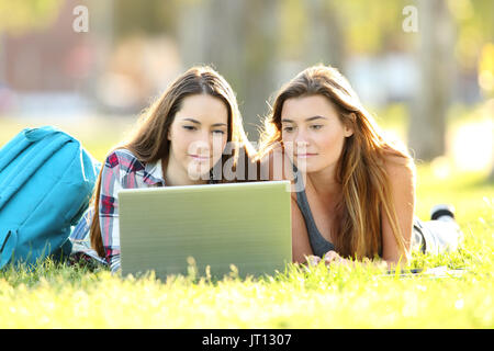 Vue de face de deux élèves, l'apprentissage en ligne avec coffre allongé sur l'herbe dans un campus universitaire Banque D'Images